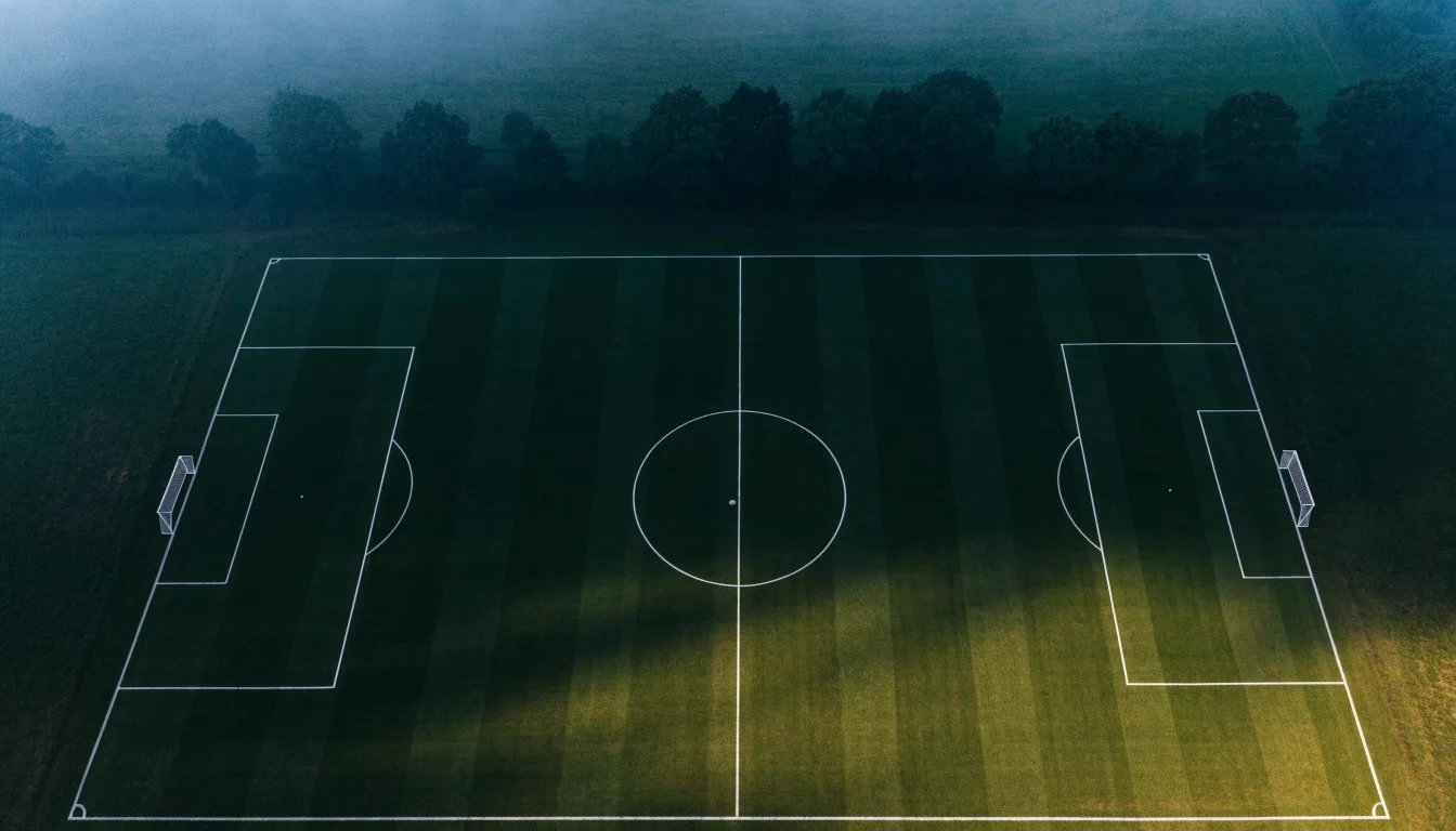 Ein Fussballplatz von oben gesehen, die Linien bilden ein helles Muster auf dem Rasen, Drohnenperspektive in der Morgendämmerung.