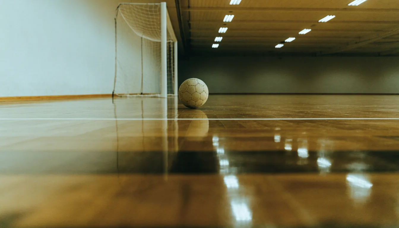 Ein Handballtor in einer leeren Sporthalle, der Ball liegt im Torraum und das Hallenlicht spiegelt sich im Parkett.