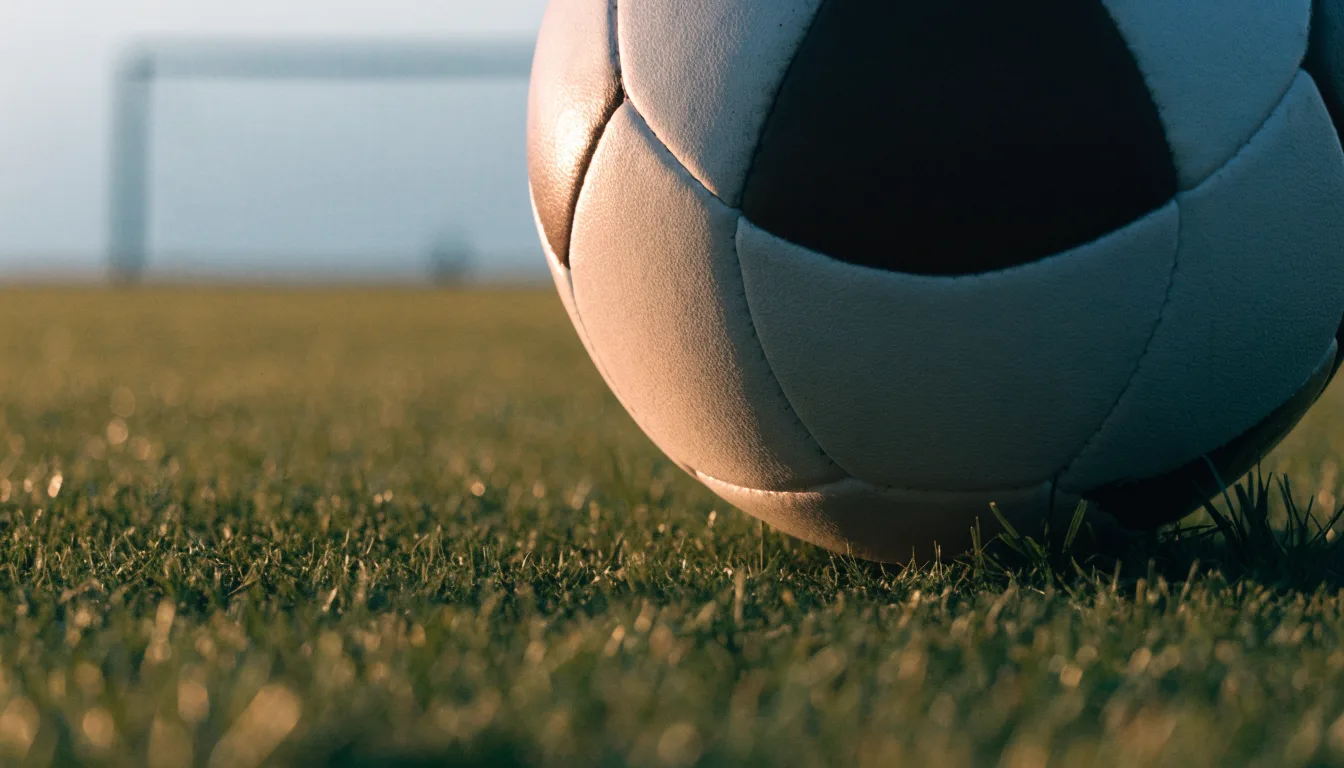 Ein Fussball auf dem Rasen aus niedriger Perspektive aufgenommen, die Torpfosten verschwimmen im Hintergrund.