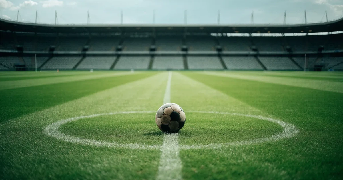 Ein Fussball liegt auf dem Anstosspunkt eines frisch gemähten Rasens, dahinter eine grosse Tribüne unter bewölktem Himmel