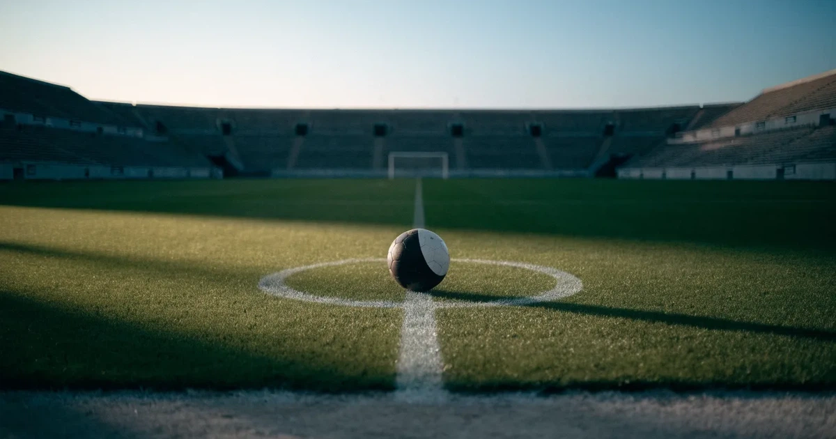 Ein Fussball liegt auf dem Mittelpunkt eines leeren Rasens, im Hintergrund steigen steile Tribünen in der Dämmerung auf.