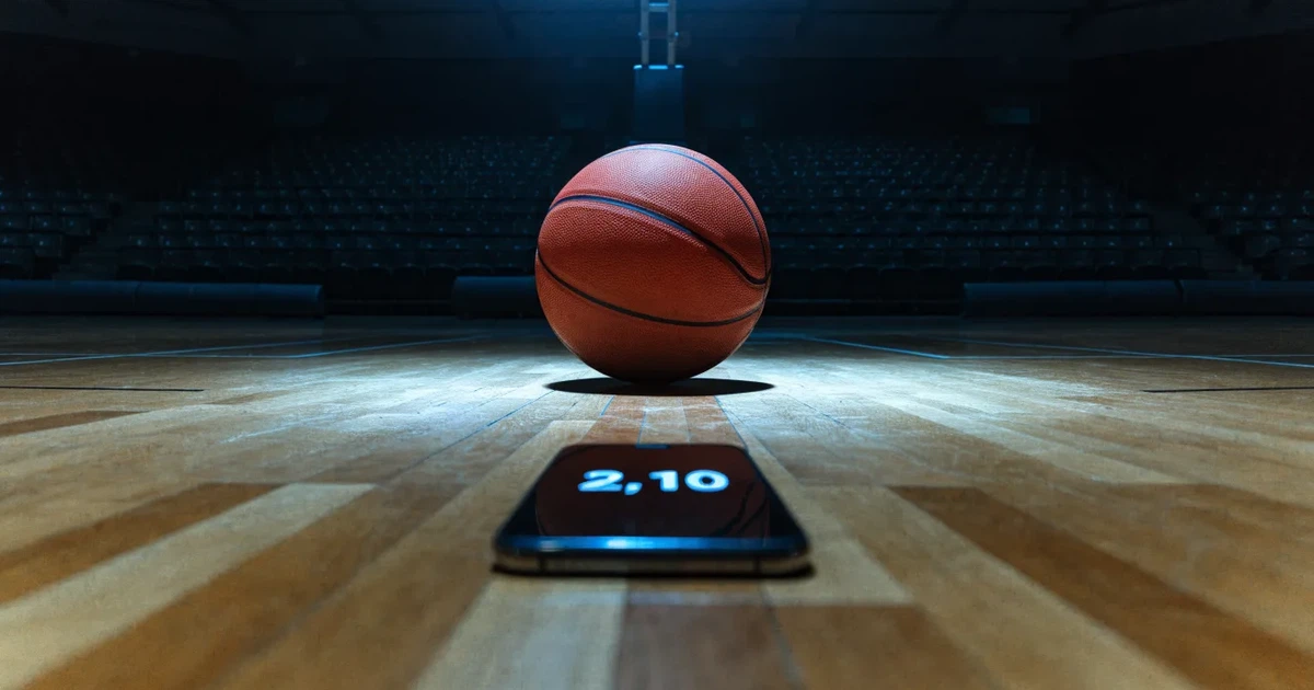 Ein orangefarbener Basketball liegt auf dem Parkett einer leeren Halle unter hellem Flutlicht, die Tribünen sind dunkel.