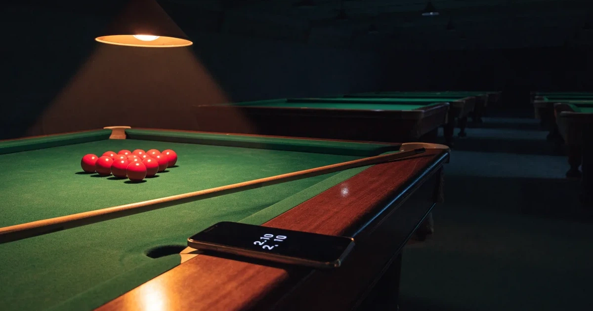 Ein Snookertisch mit grünem Tuch und einem Dreieck aus roten Kugeln unter einer tief hängenden Lampe in einer leeren Halle.