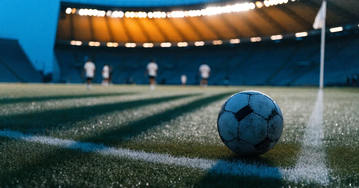Eine Seitenlinie aus weisser Kreide auf dem Rasen in der Dämmerung, in der Ferne ragt eine hell beleuchtete Stadionschüssel auf.